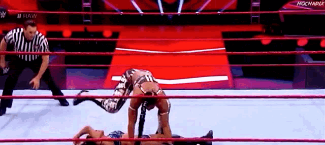 two wrestlers are wrestling in a ring with a referee in the background .