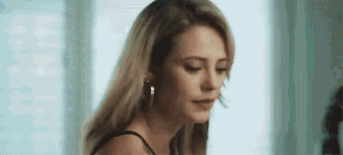 a close up of a woman wearing a black top and earrings looking at the camera .