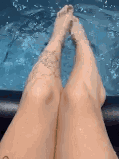 a woman with tattoos on her legs is sitting in a pool .