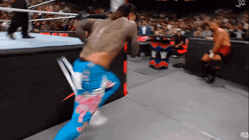 a wrestler in blue and pink pants is running across the ring
