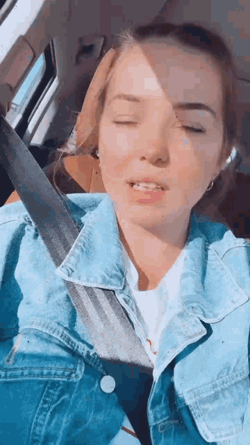 a woman is wearing a denim jacket and a seat belt while sitting in a car .