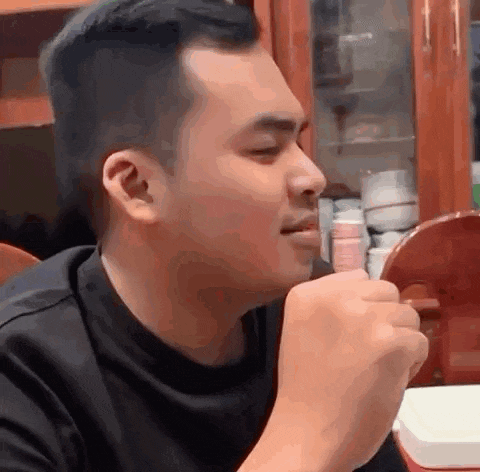 a man in a black shirt is sitting at a table with his fist in his mouth .