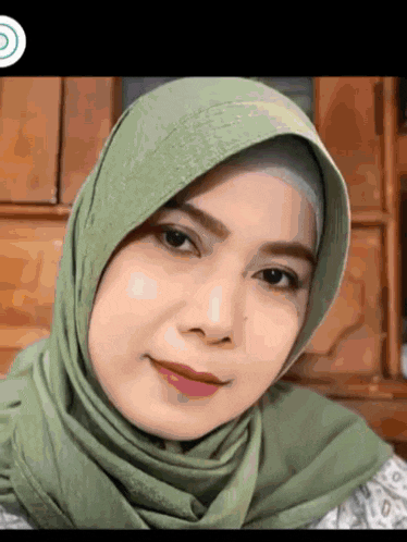 a woman wearing a green hijab looks at the camera and smiles