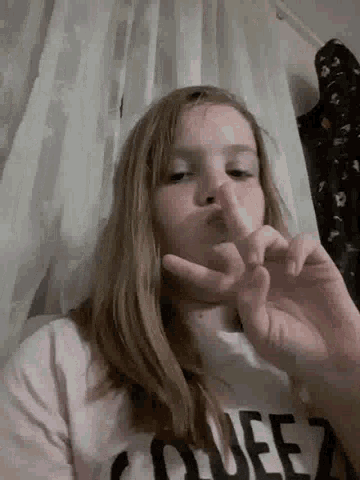 a young girl is making a peace sign with her hands while laying on a bed .