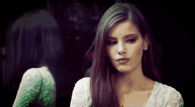 a woman with long hair is looking at her reflection in a mirror .