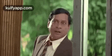 a man in a suit and tie is standing in front of a window .
