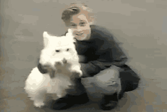 a young boy is kneeling down with a white dog .