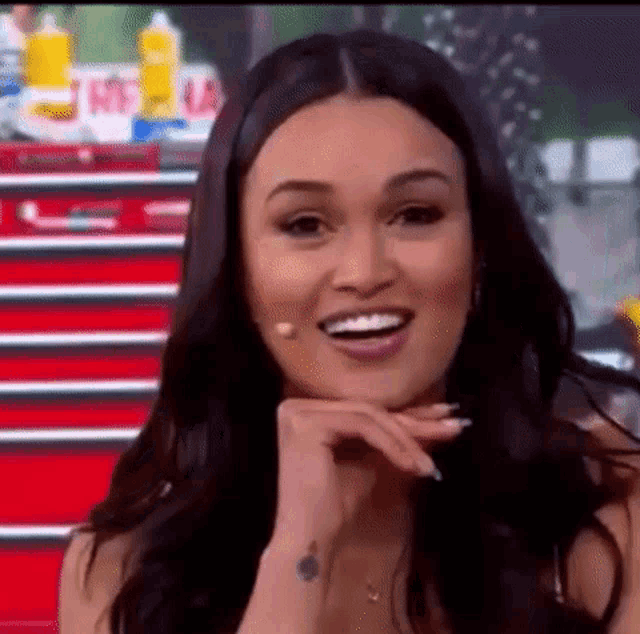 a woman is smiling with her hand on her chin while sitting in front of a microphone .