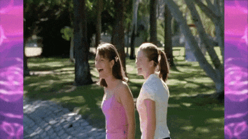 two young girls are laughing while walking in a park .