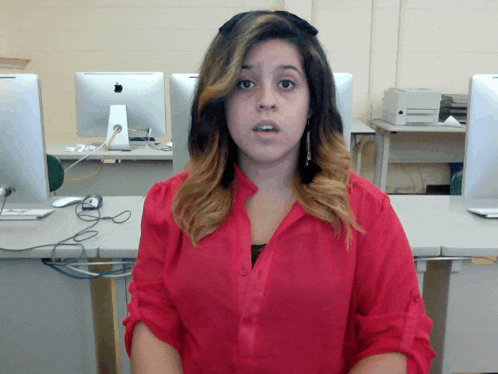 a woman in a red shirt is standing in front of a computer monitor