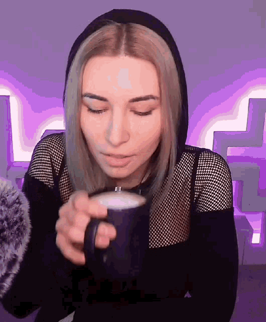 a woman wearing a black hoodie is drinking from a purple mug .