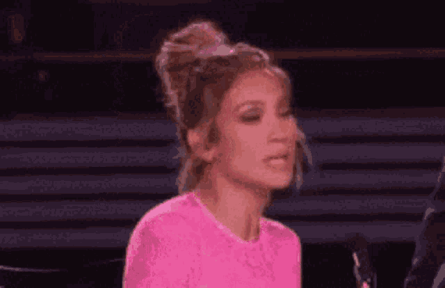 a woman in a pink shirt is sitting in front of a microphone and making a face .