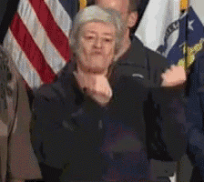 a woman in a black jacket is standing in front of a group of people with flags in the background