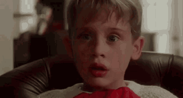 a young boy is sitting in a chair wearing a red bow tie and a sweater .