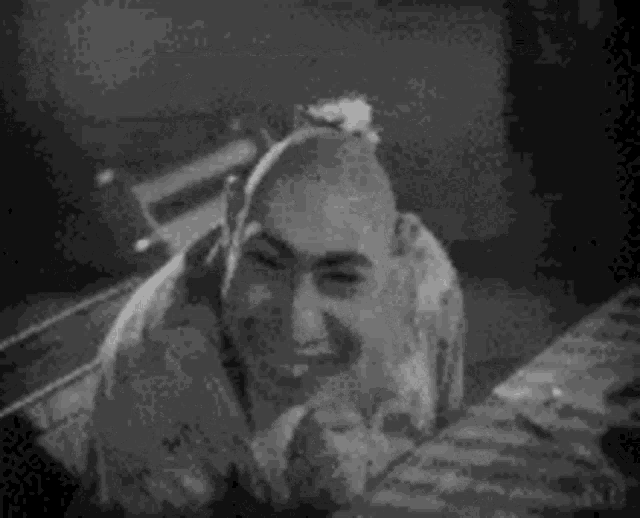 a black and white photo of a woman sitting on a bed looking at herself in the mirror .
