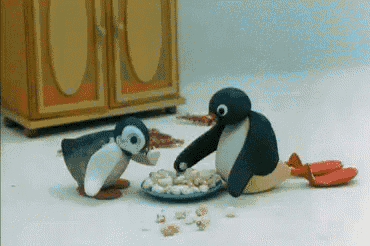 two stuffed penguins are eating from a plate on the floor