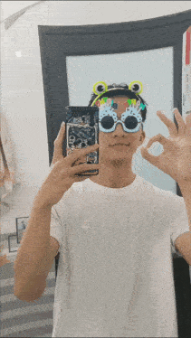 a man wearing frog glasses takes a selfie in a mirror