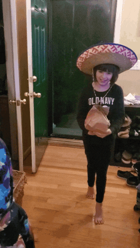 a girl wearing a sombrero and an old navy shirt holds a box