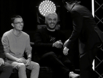 a man is kissing another man on the cheek while sitting on a stage .