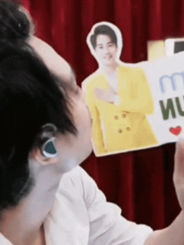a man wearing ear buds kisses a cardboard cut out of a man in a yellow jacket