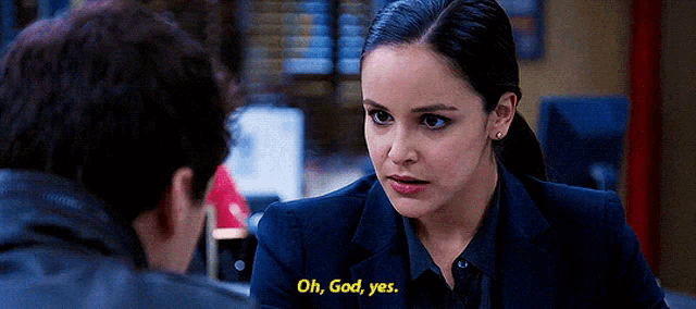 a woman in a suit is talking to a man in a leather jacket and says oh god yes