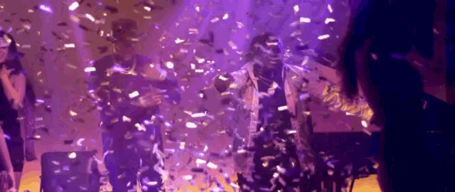 a group of people are dancing on a stage with confetti falling