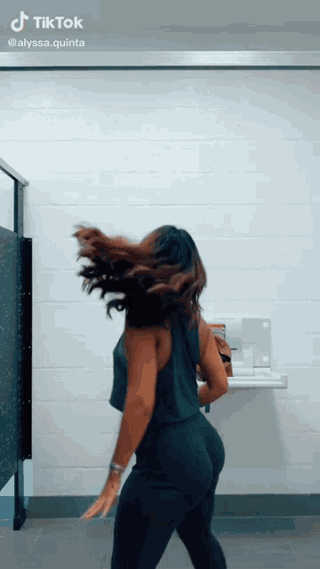 a woman in a black tank top and black pants is dancing in a public restroom .
