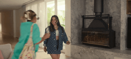 two women are standing in a living room with a fireplace