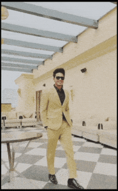 a man in a yellow suit and black shirt is standing in a room with a checkered floor