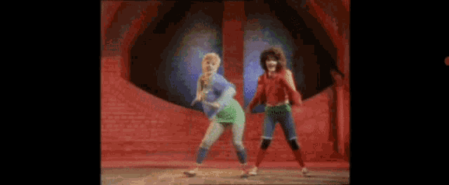two women are dancing on a stage in front of a brick wall in a room .