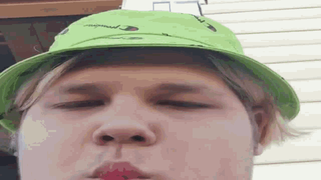 a man wearing a green hat and red lipstick is blowing a bubble .