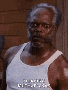 a man with a beard is wearing a white tank top and looking at the camera .
