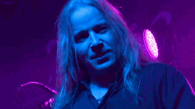 a man with long hair is screaming in front of a blue and purple light