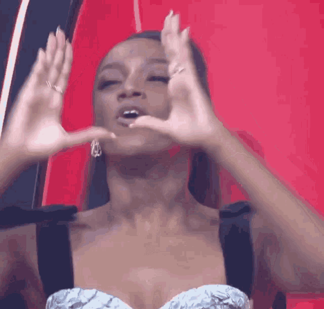 a woman in a silver and black dress is making a heart shape with her hands