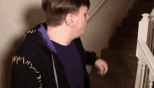 a man in a purple shirt and a black jacket is walking down stairs .