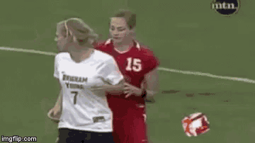 two female soccer players are standing next to each other on the field .