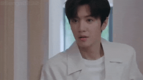 a young man in a white coat is standing in a room looking at the camera .