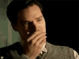 a close up of a man covering his mouth with his hand in a dark room .