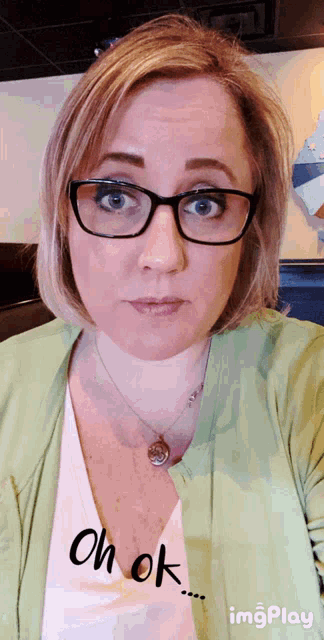 a woman wearing glasses and a green cardigan says " oh ok "