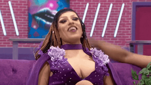 a woman in a purple dress is sitting on a purple couch and smiling