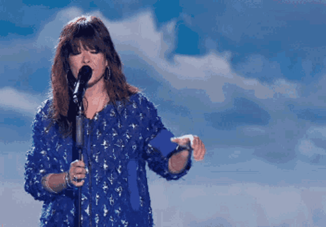 a woman singing into a microphone with a blue background