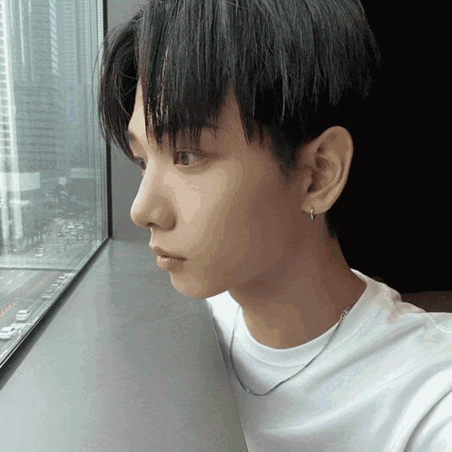 a young man in a white shirt is looking out of a window