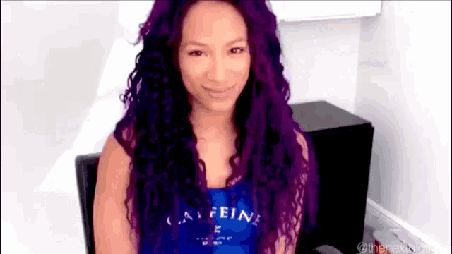 a woman with purple hair is wearing a blue tank top with the word caffeine on it .