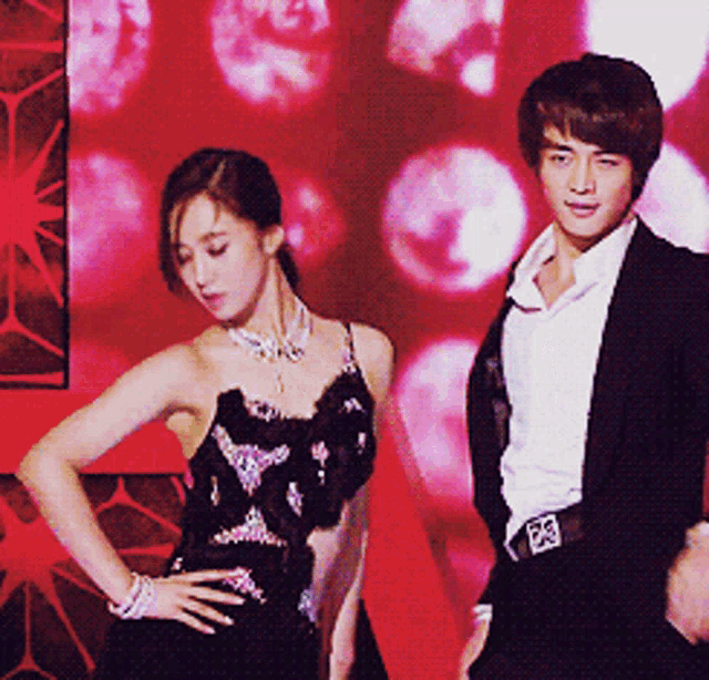 a woman in a black dress is standing next to a man in a suit with the number 23 on his belt
