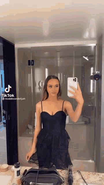 a woman in a black dress is taking a selfie in the bathroom mirror .