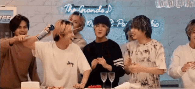 a group of young men standing around a table with a neon sign that says the grande