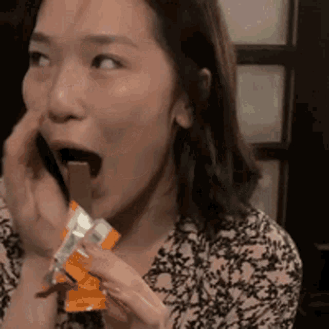 a woman in a pink shirt is eating a chocolate bar