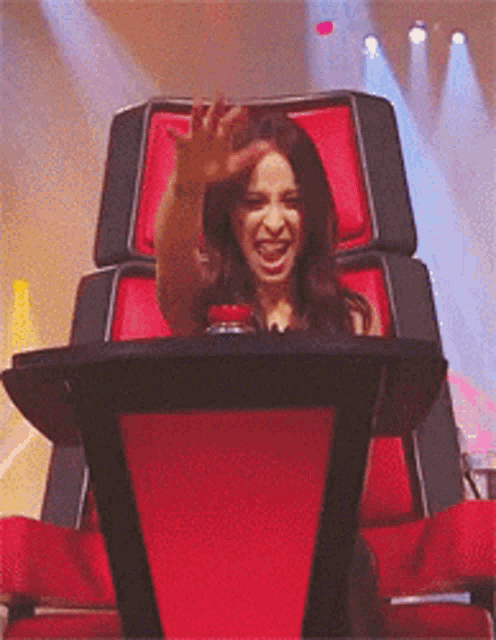 a woman is sitting in a red chair with her hand in the air