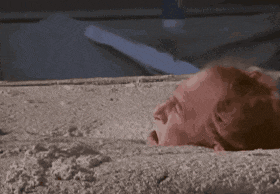 a man is laying in the sand and looking out of a hole .