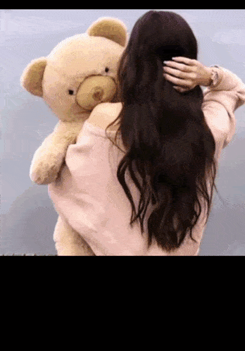 a woman is holding a teddy bear in her arms and touching her hair